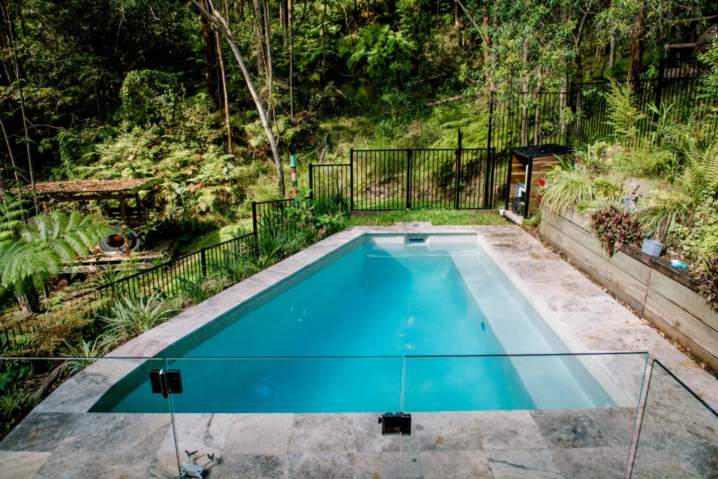 A backyard pool with retaining wall pools made by aqua living pools nestled amidst lush trees, creating a serene oasis.